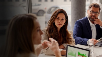 A man and woman sit at a desk and listen to another woman speak 