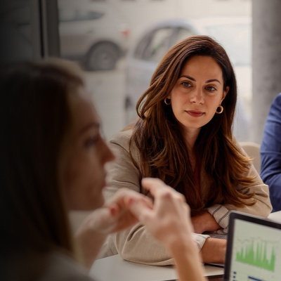 A man and woman sit at a desk and listen to another woman speak 