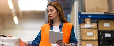 Woman with tablet in warehouse wearing safety vest.