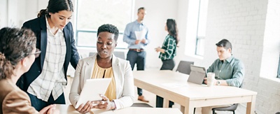 Three co-workers, in an open and bright office space, review a project on a tablet computer. 