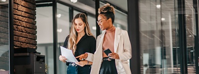 two-women-walking-in-office-reading-paper