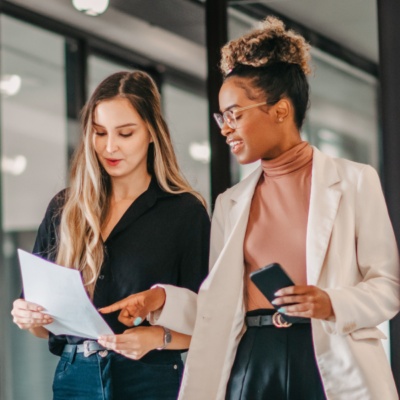 two-women-walking-in-office-reading-paper