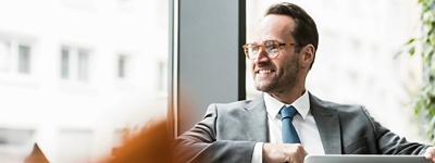 An executive with a laptop looking out the window smiling.