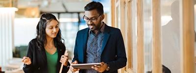 Two HR colleagues walking down an office corridor while looking at an iPad.