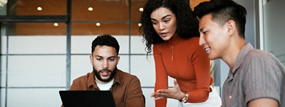Coworkers looking at laptop woman standing and referencing screen