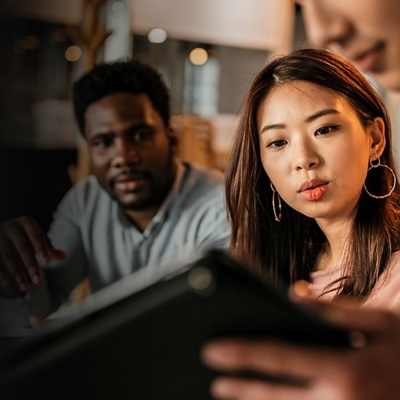 A male and female employee look at a tablet that a co-worker is holding up for them.