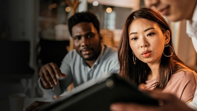 A male and female employee look at a tablet that a co-worker is holding up for them.