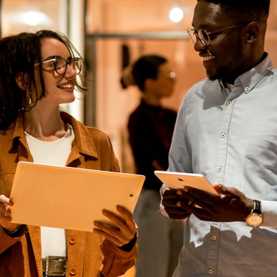 Coworkers with glasses smiling at each other while holding tablets