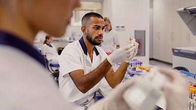 Image of a man working in a lab looking at test tubes that he is holding