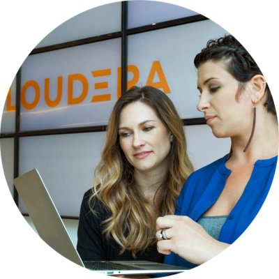 Zwei Mitarbeiterinnen bei Cloudera, die auf einen Laptop schauen