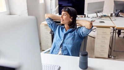 An image of a woman sitting in front of a computer with her hands folded behind her head