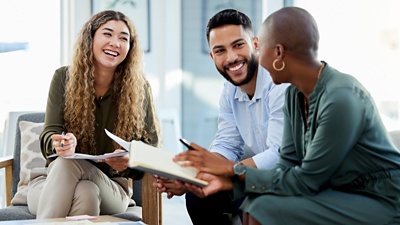 Image of three people sitting and smiling at each other while working