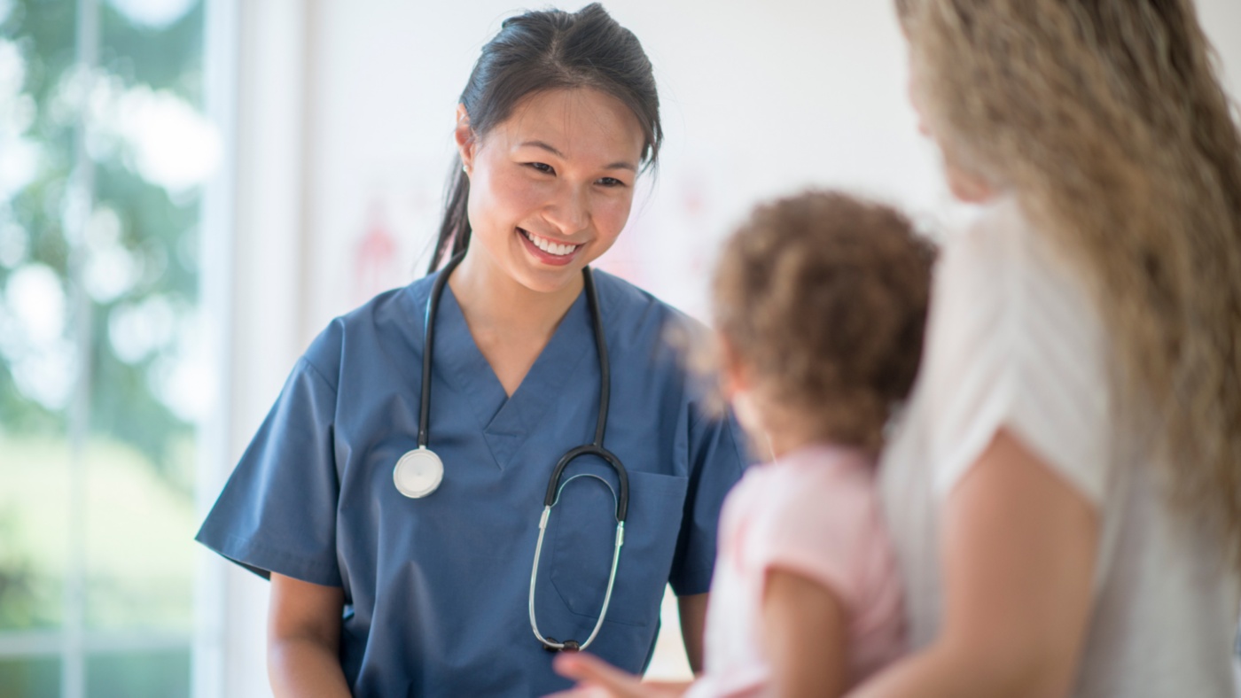 Image of a female doctor or nurse looking at a woman holding a small young girl