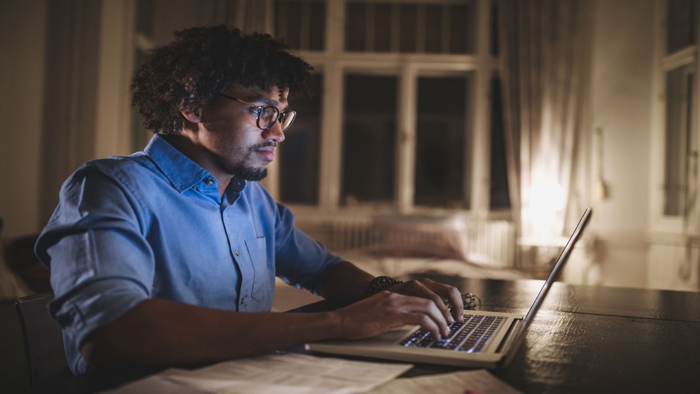 Young and determined black student studying at night at home, with a help of a laptop computer.