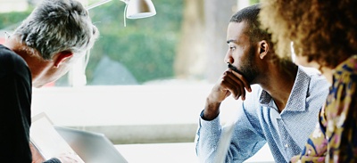 Three employees at a desk looking at a computer together.