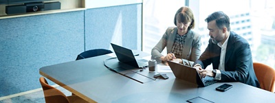 Two colleagues in a conference room referencing information on a laptop.