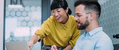 Two happy employees looking at a laptop screen together.