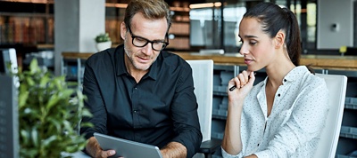 Two employees in an open office looking at a tablet. 