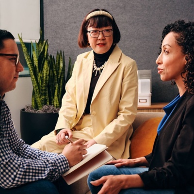 Three colleagues seated in a group discussion in a modern office, with one taking notes in a notebook.
