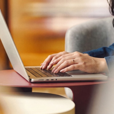 Female with long hair using laptop in office lounge area.