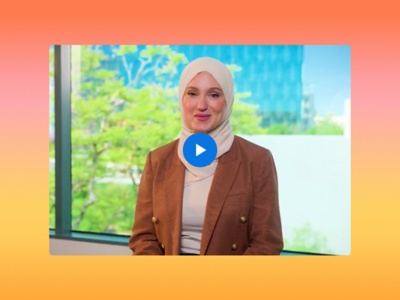 A smiling Laila Almounaier stands in a bright, modern office setting with a play button overlay.