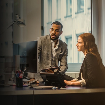 A man and woman look at a computer screen on a desk