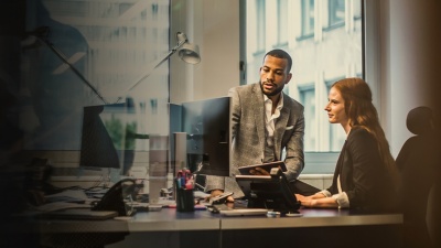 A man and woman look at a computer screen on a desk