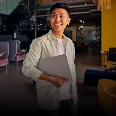 Person dressed in business casual attire in an office holding a laptop and looking to the left