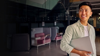 Person dressed in business casual attire in an office holding a laptop and looking to the left