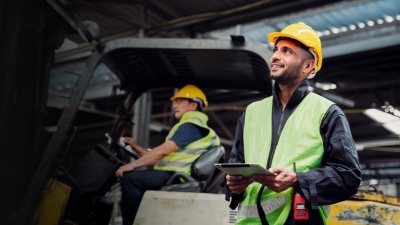 A worker at a construction site holds a tablet and looks beyond the frame