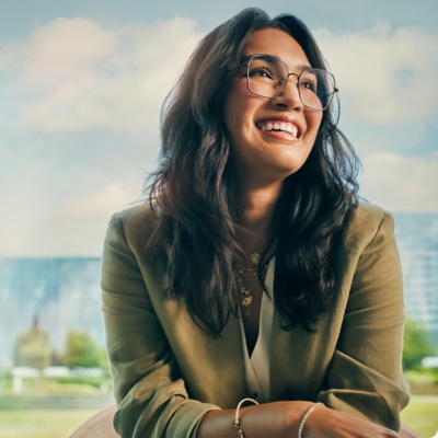 Woman in green blazer smiling with arms crossed in office.