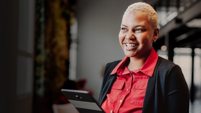 A smiling businessperson standing and holding a tablet.