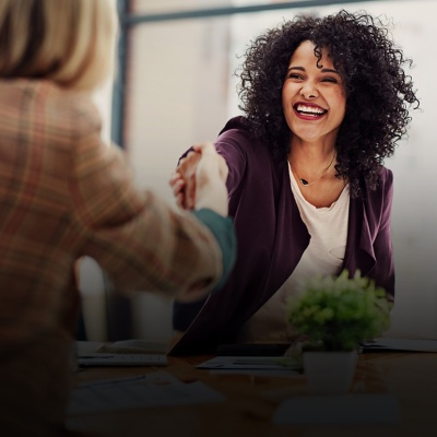 A woman smiles while shaking hands with someone else