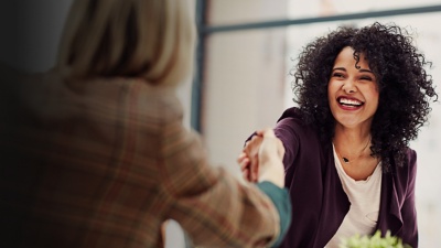 A woman smiles while shaking hands with someone else
