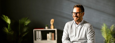 Man with glasses smiling foliage in background 