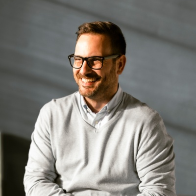 Man with glasses smiling foliage in background 