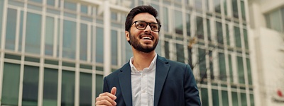 Man with glasses smiling in front of buildings