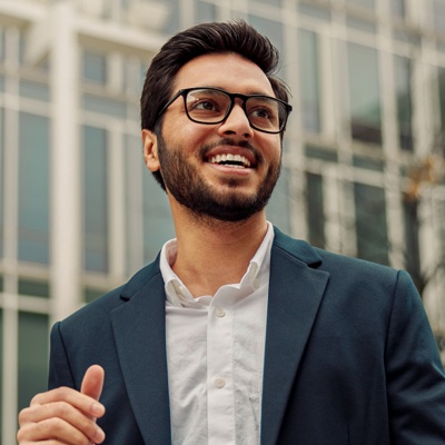 Man with glasses smiling in front of buildings