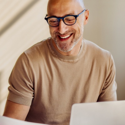Man with glasses smiling looking at paper with laptop open