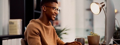 Man with glasses smiling sitting at desk looking at monitor