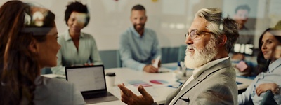 Man with glasses talking to woman at table with colleagues