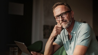 A man sits at a table holding an iPad while looking at the camera.   