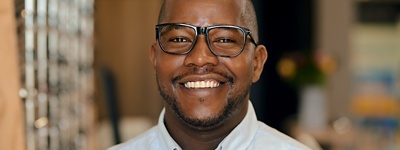 Man with glasses and button-up shirt smiling at the camera