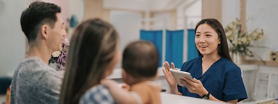 nurse at desk with tablet looking at family in doctor office