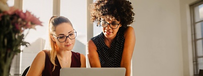 Two colleagues collaborating over a laptop in a bright office