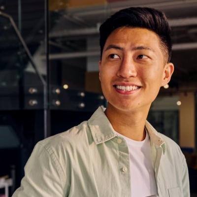Portrait of a cheerful young asian man holding a laptop in a modern office environment.