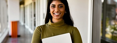 Person smiling directly into camera holding laptop