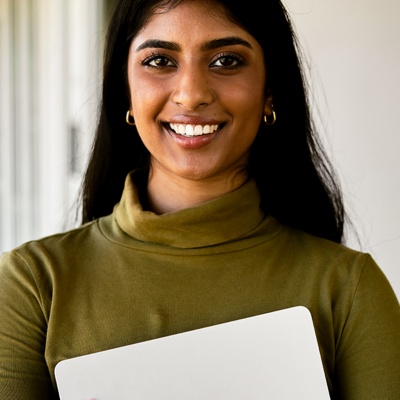 Person smiling directly into camera holding laptop