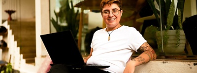 Person with glasses smiling and sitting with laptop on lap