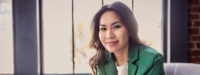 An SMB leader sitting on a couch with her phone, smiling at the camera.